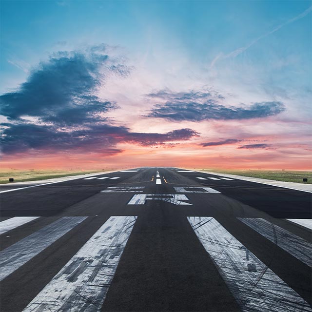 Runway threshold markings under a colourful sunset sky